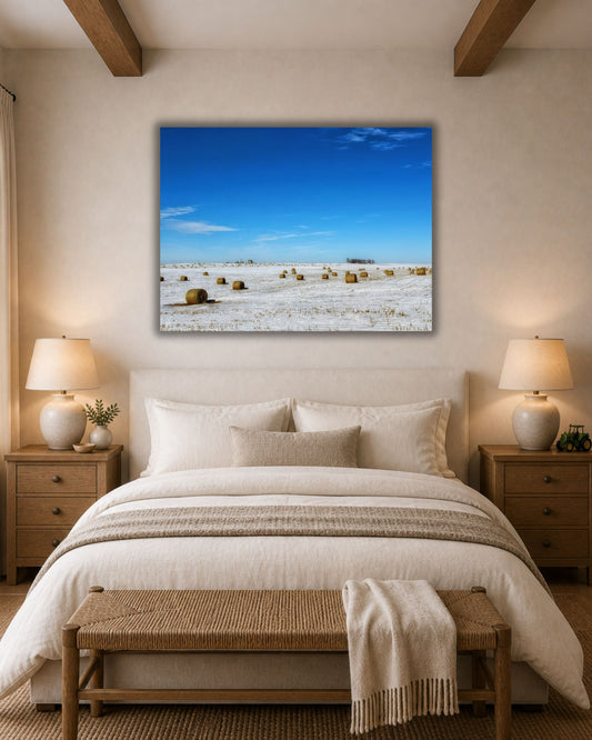 Snowy hay bale field canvas wall art displayed above a bed in a warm neutral farmhouse-style bedroom.