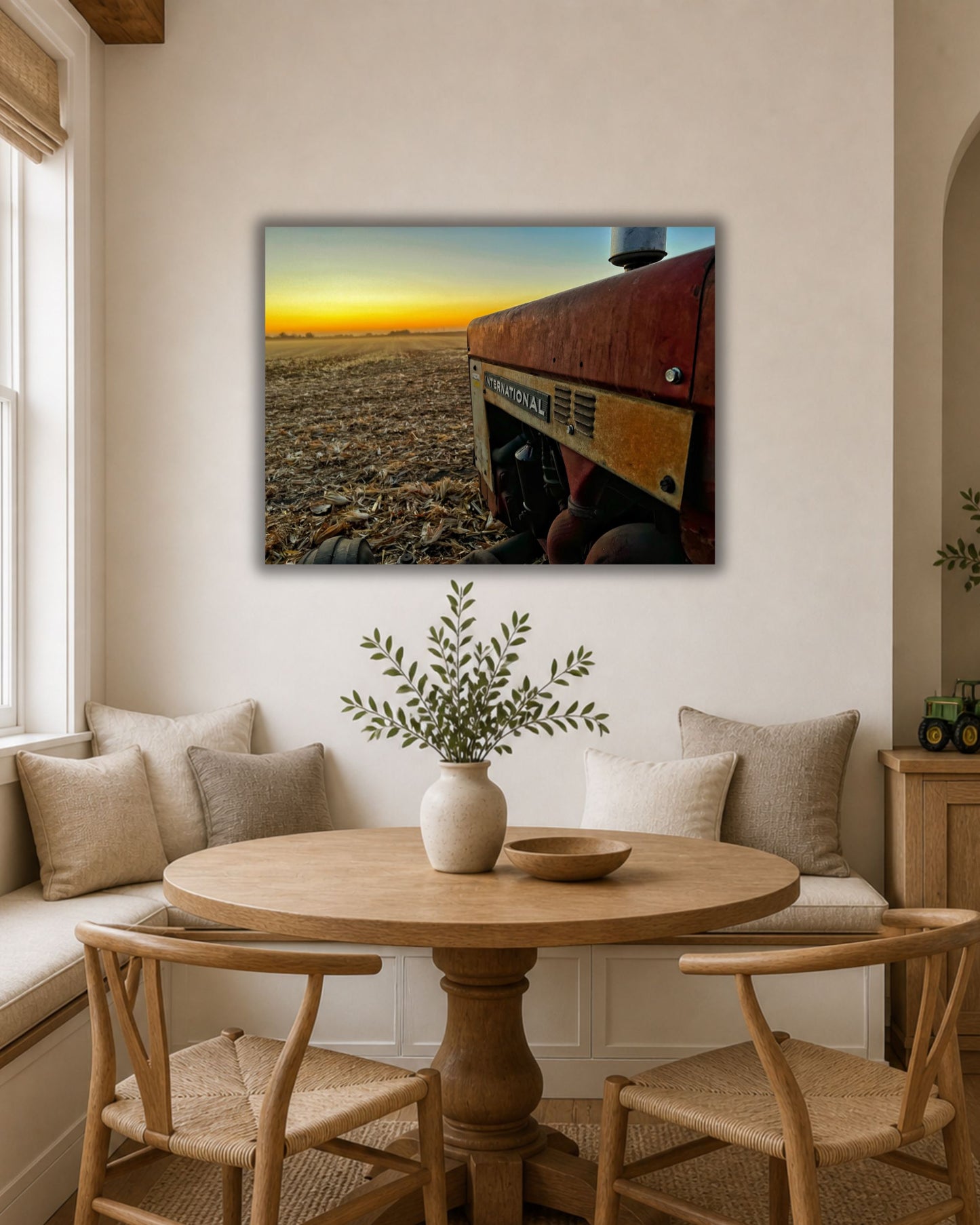 Natural oak framed International tractor harvest sunset canvas displayed above two neutral accent chairs in a warm farmhouse sitting area.