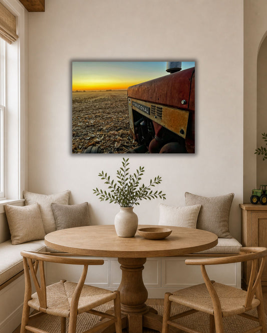 Natural oak framed International tractor harvest sunset canvas displayed above two neutral accent chairs in a warm farmhouse sitting area.