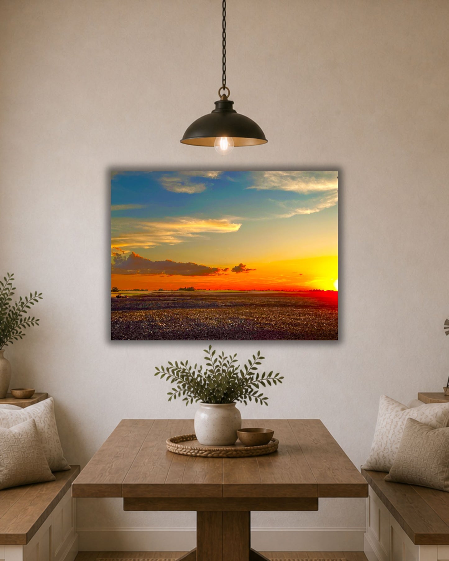 Natural oak framed rural sunset wall art displayed between two cream accent chairs in a cozy neutral sitting area.