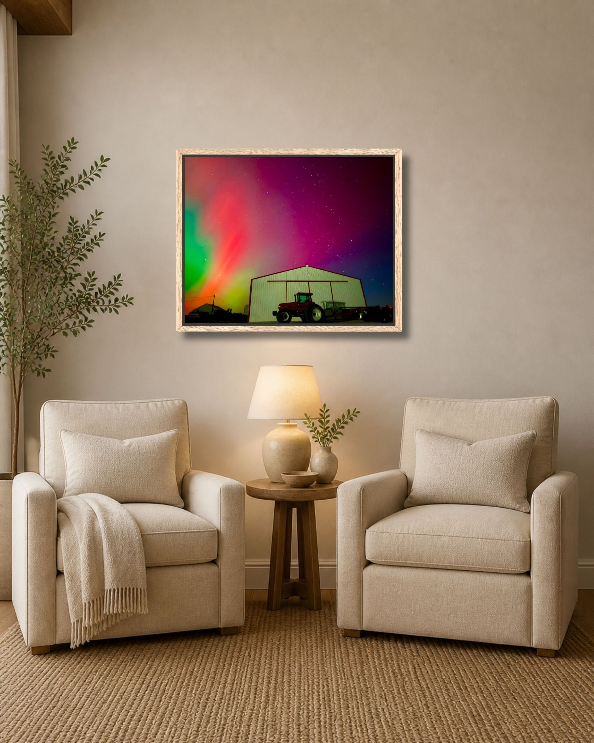 Natural oak framed northern lights farm wall art displayed between two cream armchairs in a soft neutral sitting area.