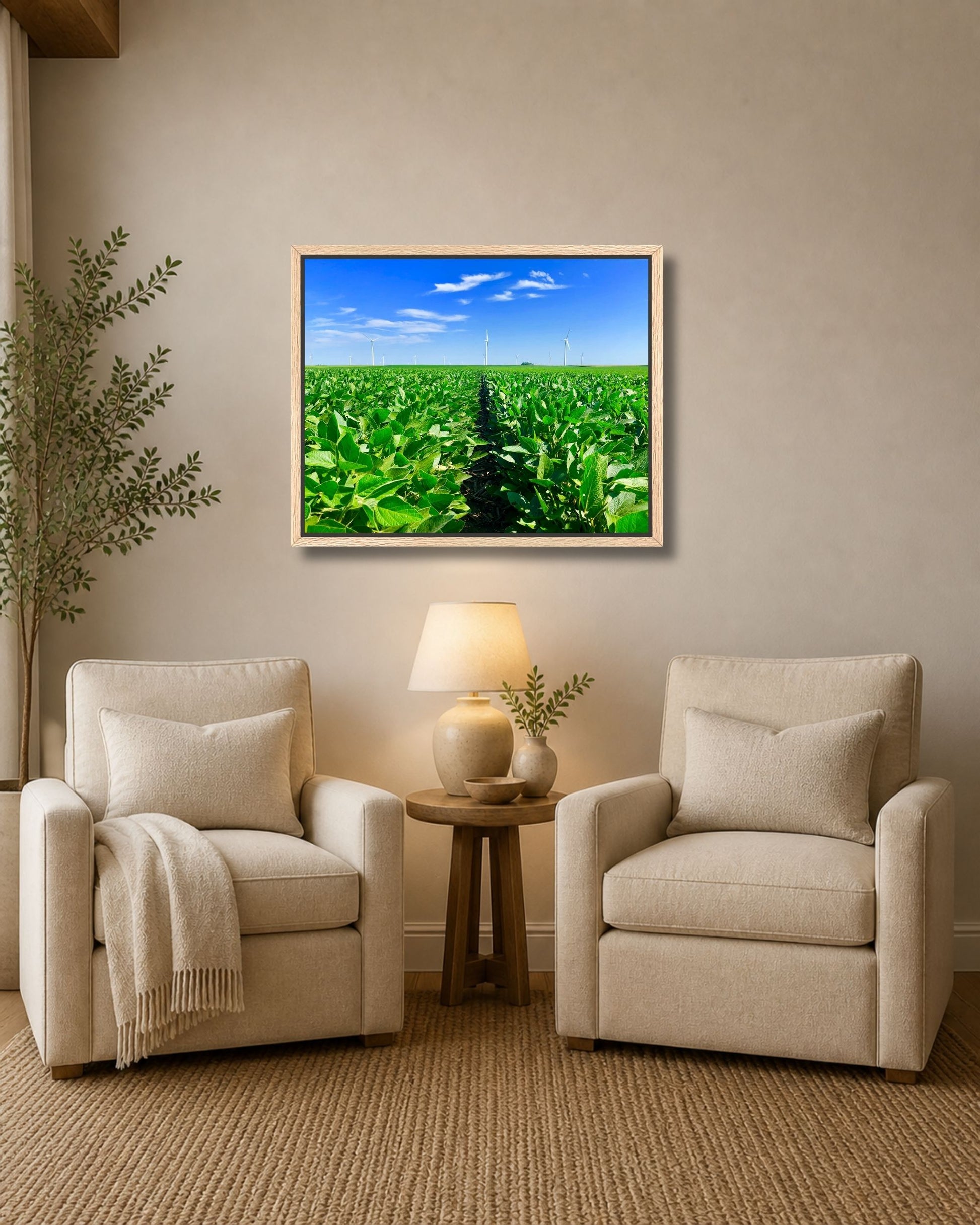 Natural oak framed soybean field and wind turbines wall art displayed above two neutral accent chairs in a cozy sitting area.