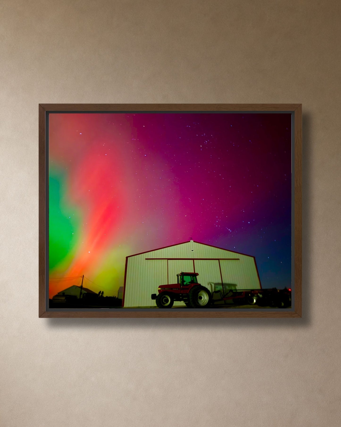 Walnut framed canvas print of vivid northern lights above a farm shed and tractor, shown in a simple close-up wall mockup.