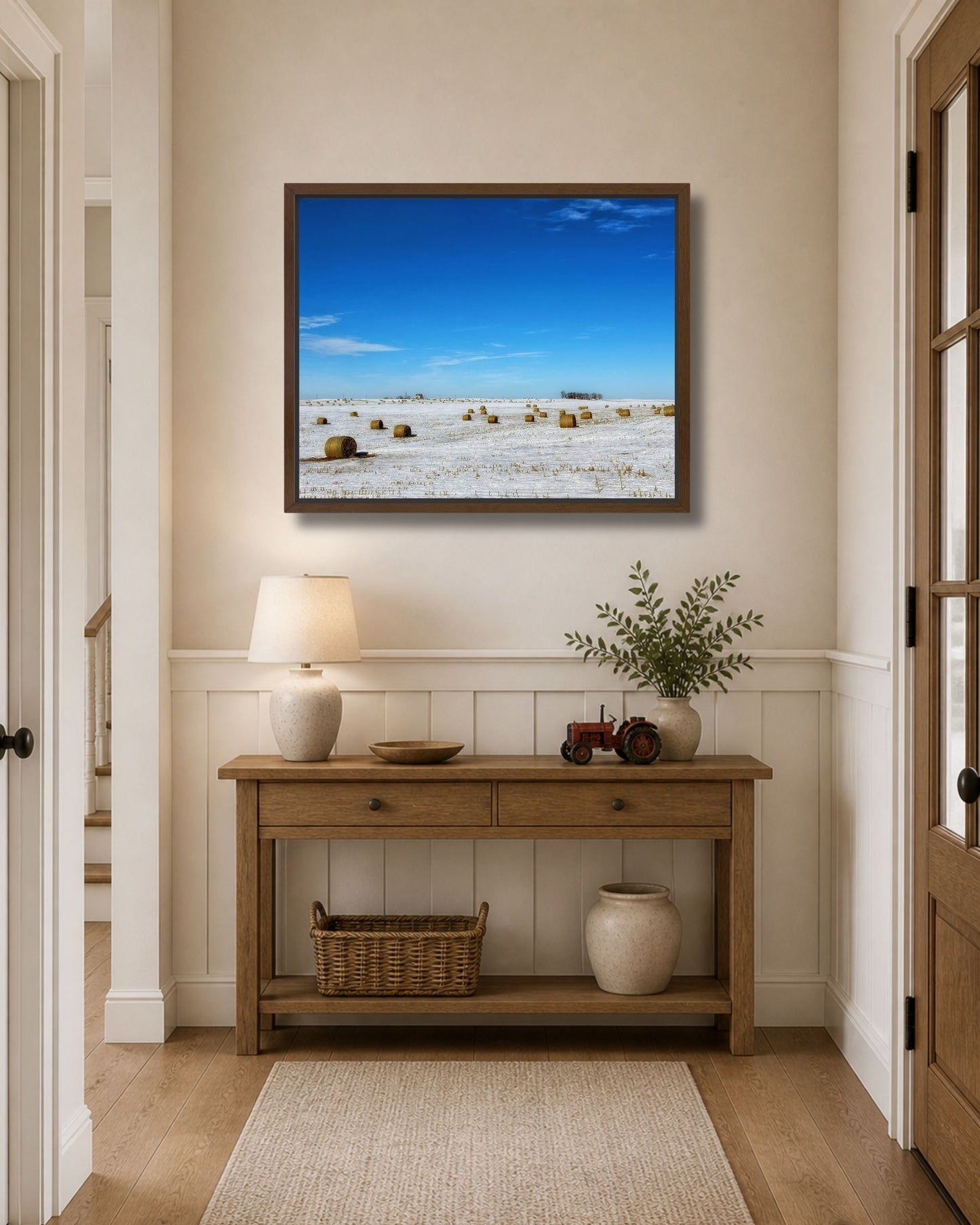 Walnut framed snowy hay bale canvas wall art styled above an entryway console table with rustic farmhouse decor.