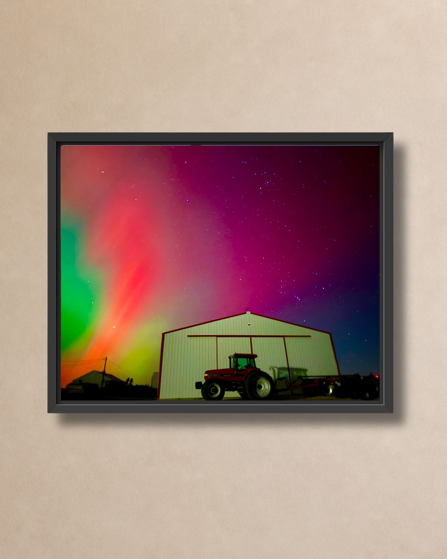 Black framed canvas print of colorful northern lights glowing above a rural farm shed and tractor.