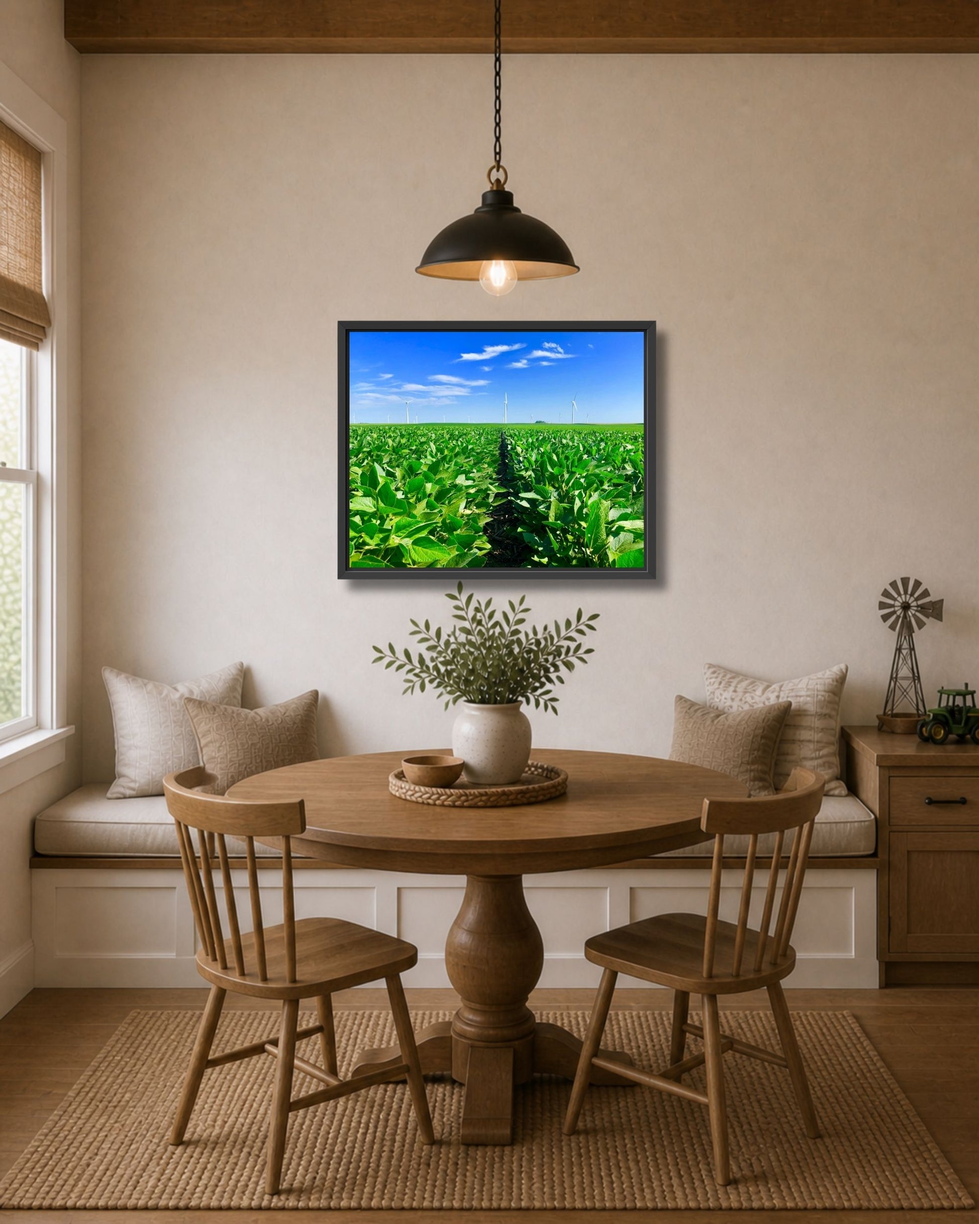 Black framed soybean field and wind turbines wall art displayed above a farmhouse dining nook with a round wood table.