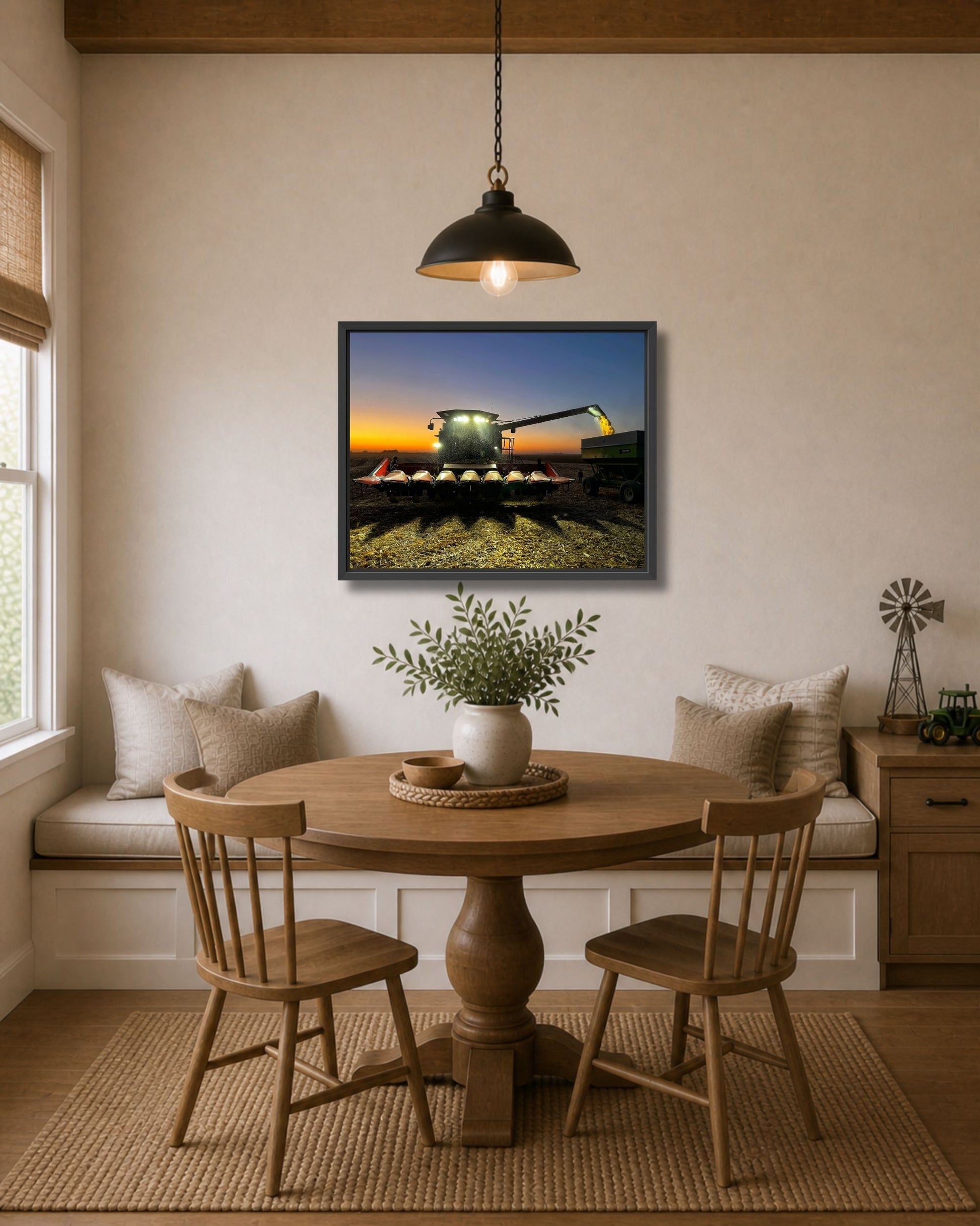Black framed combine harvest wall art displayed above a round wood dining table in a cozy farmhouse nook.