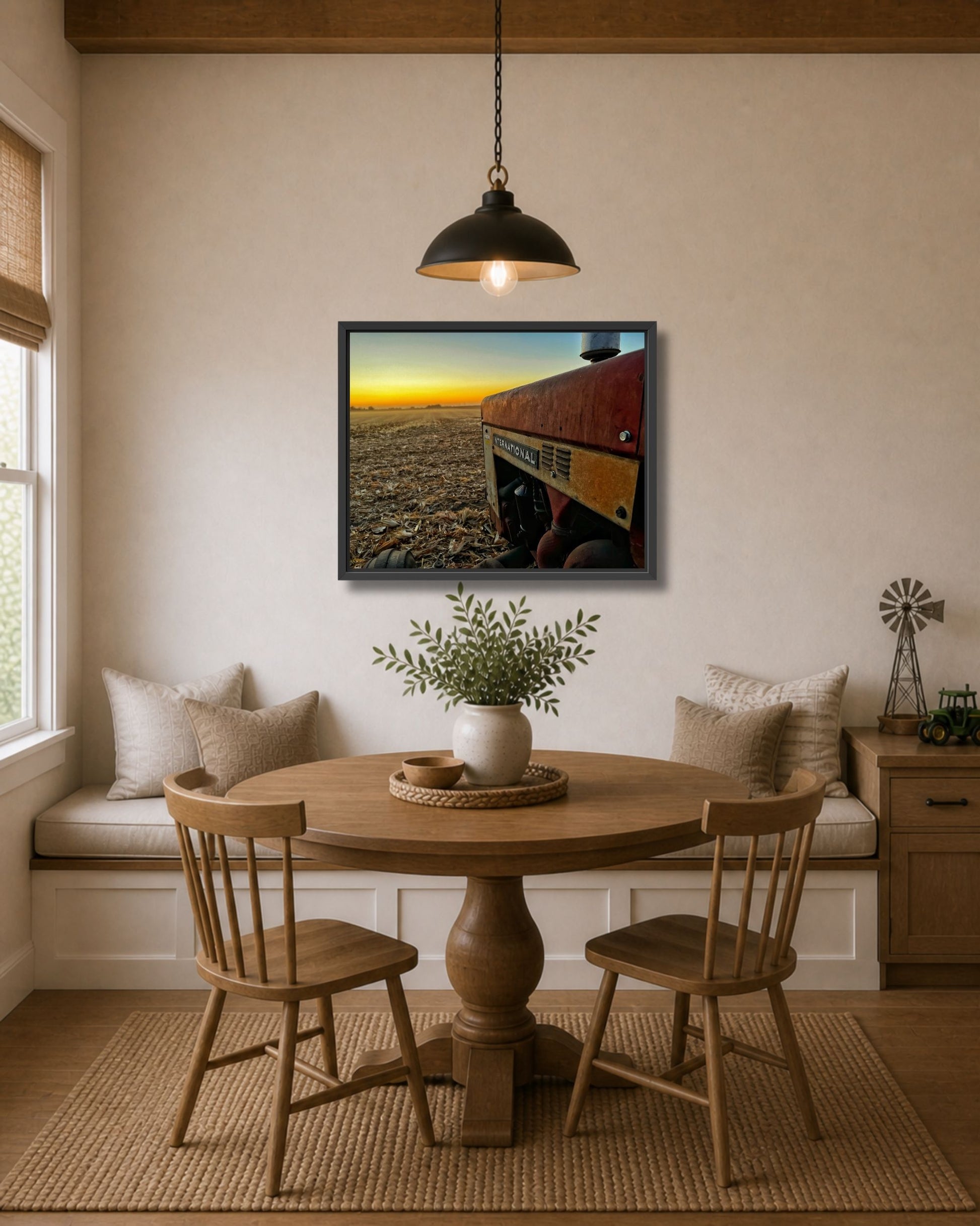 Black framed International tractor sunset farm canvas displayed above a round dining table in a warm neutral breakfast nook.